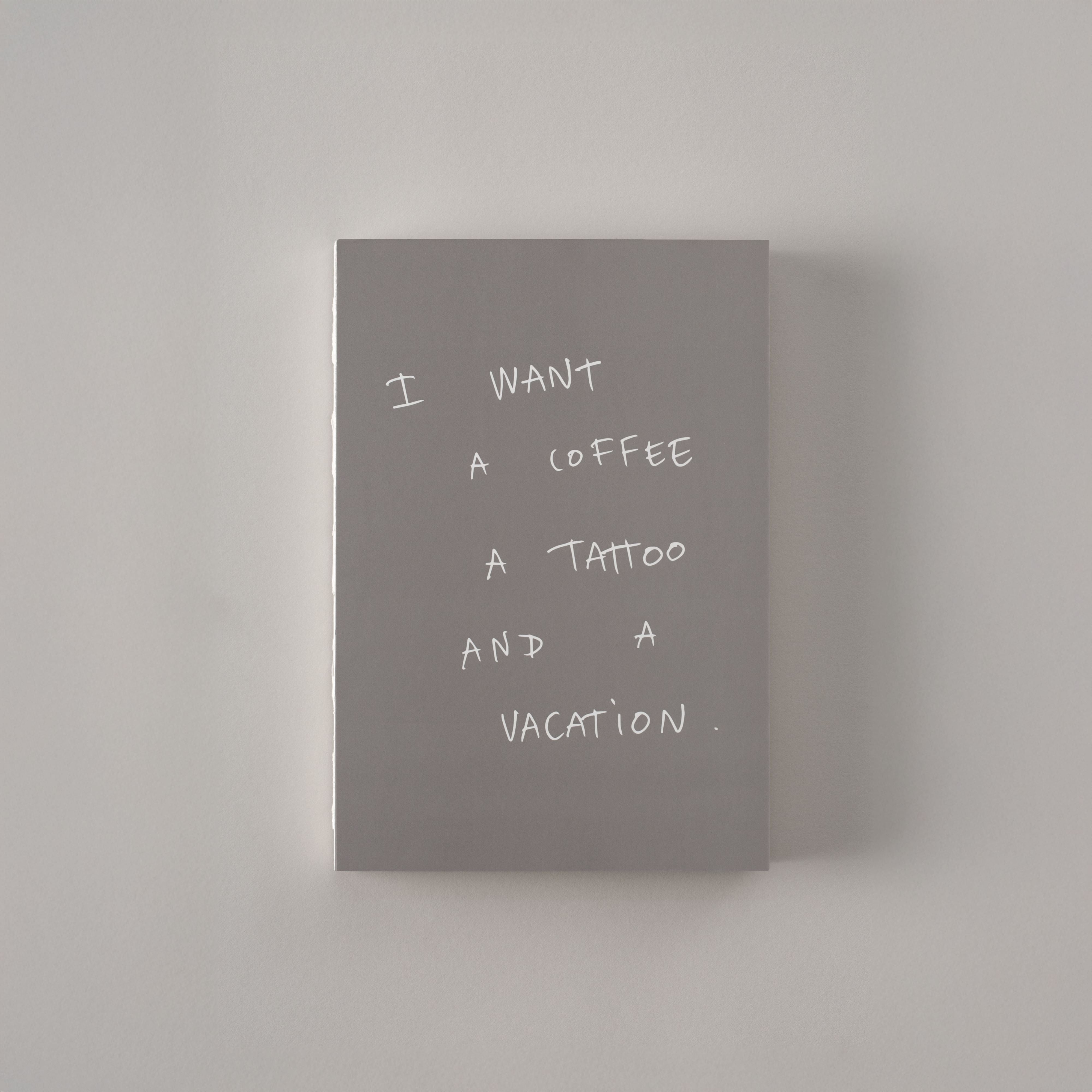 Gray notebook with text: 'I want a coffee, a tattoo, and a vacation.'