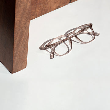 Pair of eyeglasses on a white surface next to a wooden table leg.